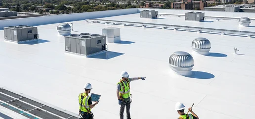 Three workers in safety vests and helmets stand on a white commercial building roof with HVAC units and vents, one pointing while another uses a laptop, highlighting Noble Roofing’s commercial roofing expertise against a cityscape backdrop.