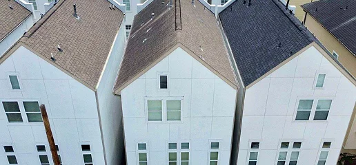 A top-down view of three modern, narrow white houses with pitched roofs by Noble Roofing, standing closely together and displaying multiple windows on each facade.