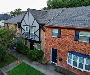 Aerial view of two townhouses, one with Tudor-style black and white trim, the other with a red brick exterior. Both have blue doors, shrubs, and sidewalks—showcasing Noble Roofing’s expertise in residential and commercial roofing services.