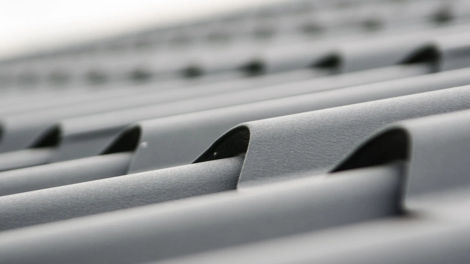 Close-up view of gray metal roofing sheets arranged in parallel lines, showing texture and wave-like pattern in soft focus—a signature look provided by Noble Roofing's expert roofing services in The Woodlands.