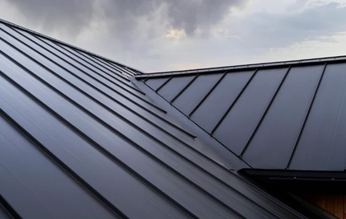 Metal roofing panels intersect at an angle, forming a modern roofline against a cloudy sky in the background. Showcasing a sleek, reflective finish, this image highlights commercial roofing expertise available in The Woodlands.
