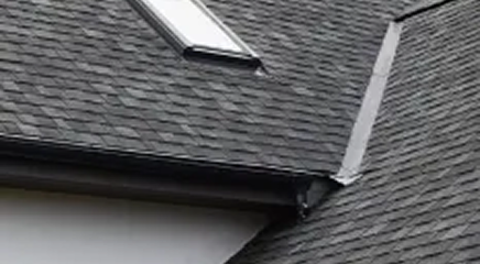 Close-up view of a modern house roof with dark gray asphalt shingles, a skylight window, and metal flashing along the roofline, showcasing quality Roofing Services by Noble Roofing.