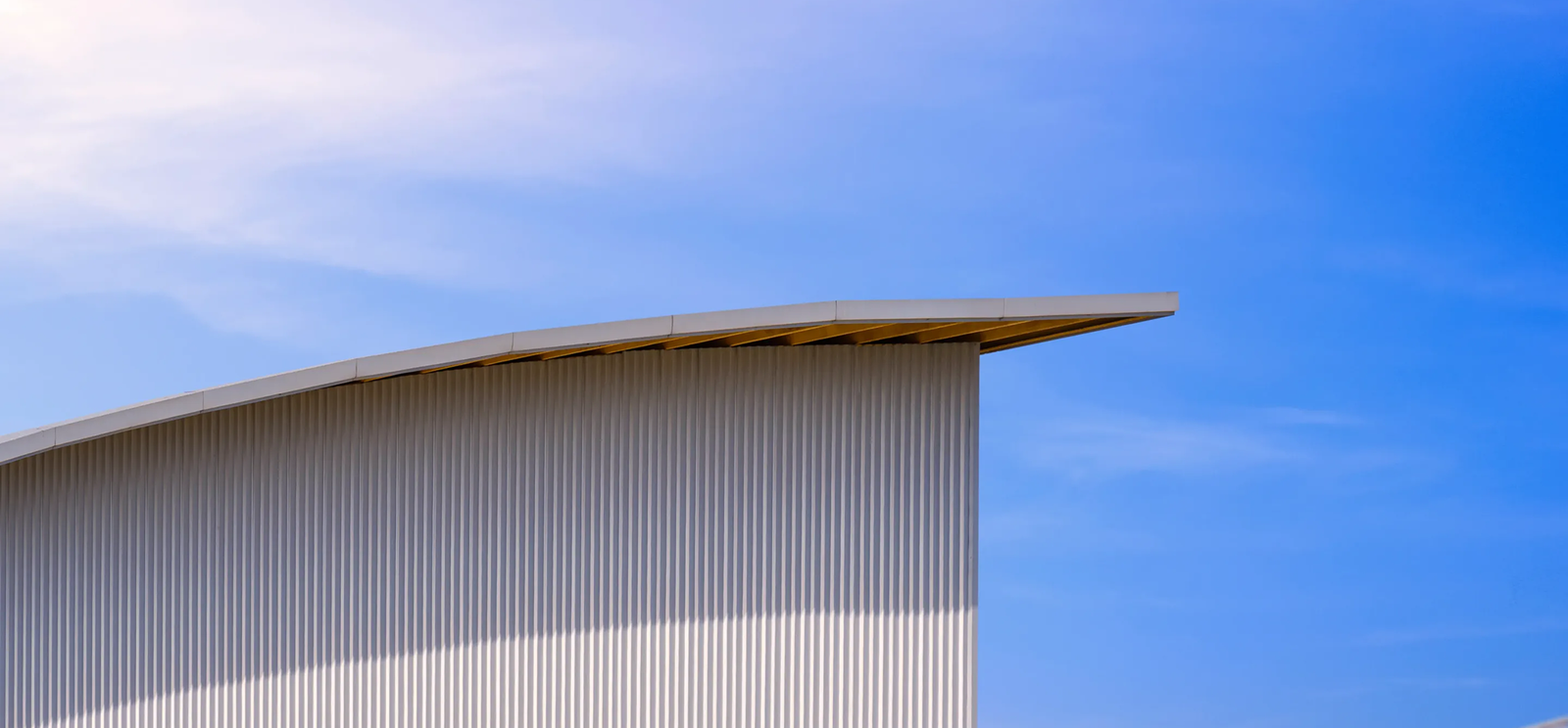 A modern commercial roofing structure in The Woodlands features a curved, ribbed metal roof and wall against a clear blue sky. Clean lines and minimalism define the design, with sunlight casting soft shadows on the building.
