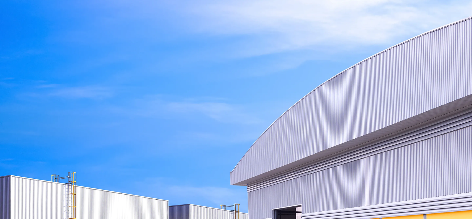 Modern industrial buildings with corrugated metal exteriors under a clear blue sky, featuring geometric rooflines and ladders, showcase top-tier Commercial Roofing in The Woodlands.