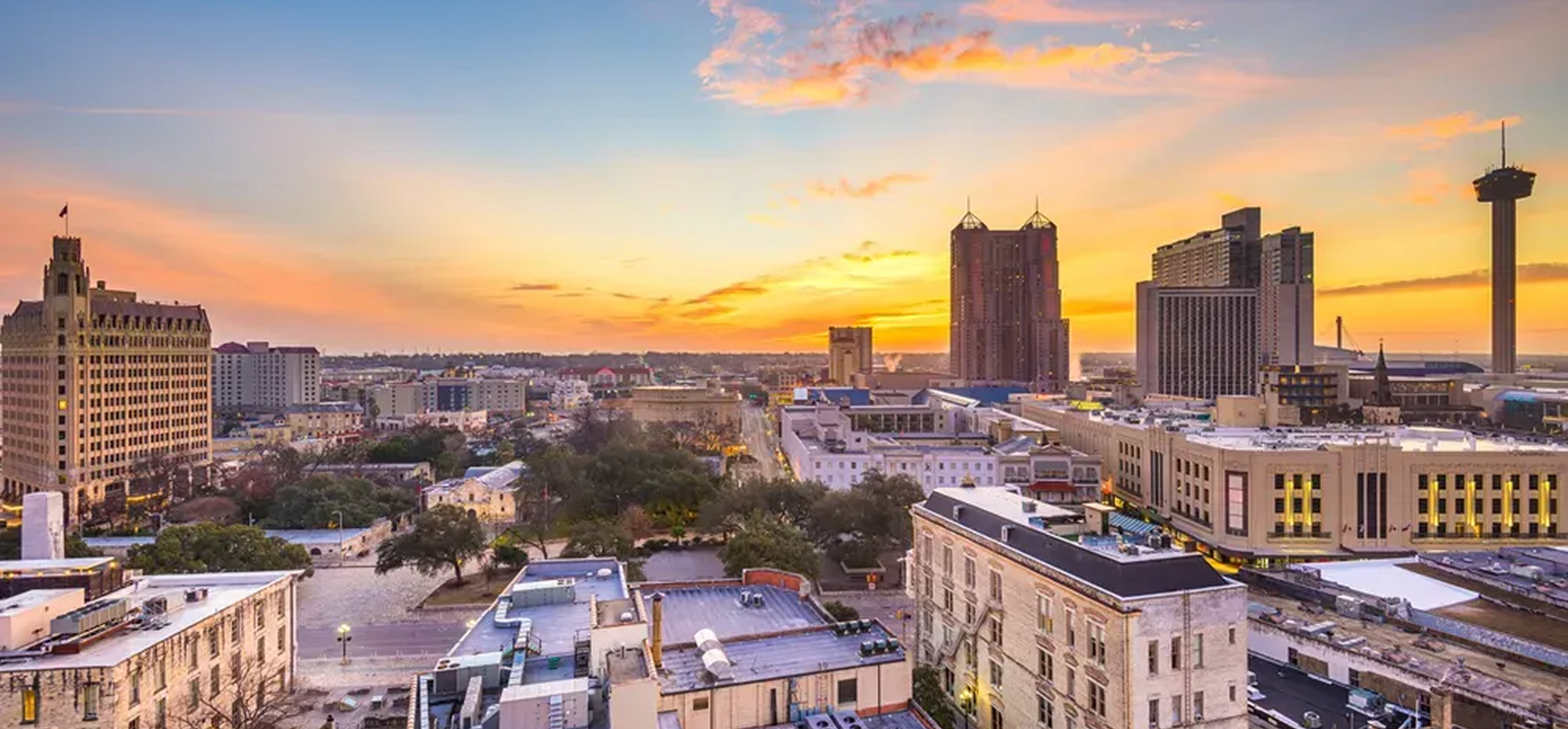 A vibrant city skyline of San Antonio, Texas at sunset, featuring tall buildings, the historic Tower Life Building, the Tower of the Americas, and a colorful sky—showcasing excellence in commercial roofing for businesses across The Woodlands.