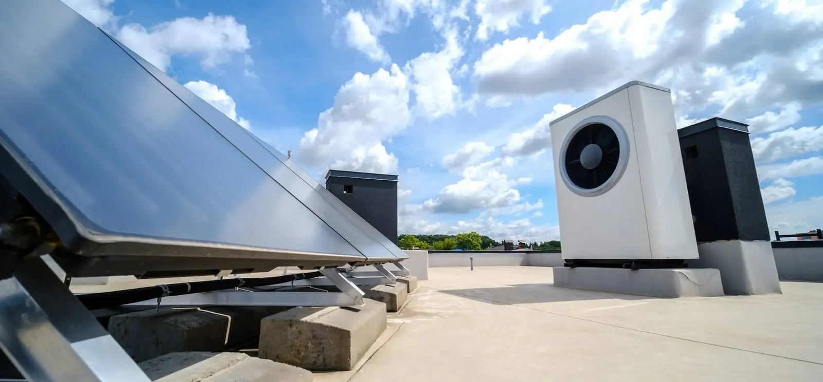 Solar panels and a large white air source heat pump are installed on a flat rooftop under a bright blue sky with scattered clouds, showcasing Noble Roofing’s commitment to renewable energy and sustainable commercial roofing in The Woodlands.