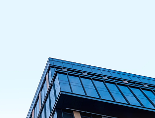 A modern glass building with blue-tinted windows in The Woodlands is shown from a low angle against a clear, pale sky, emphasizing the structure’s sleek lines and minimalist design.