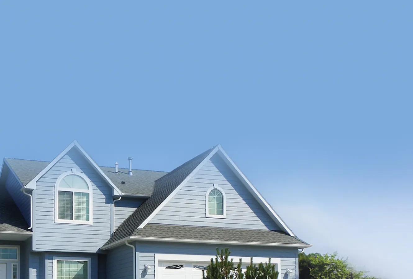 Two-story blue house with white trim, arched windows, and a gray shingle roof—expertly maintained by Roofing Services—stands partially visible under a clear blue sky with some trees in the background in The Woodlands.